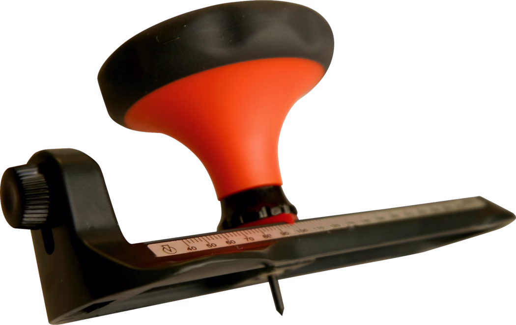WOLFF_Dummy_15624_circular cutter_2025-08 Nahaufnahme eines handgehaltenen Holzbearbeitungswerkzeugs (möglicherweise Schleifgerät oder Hobel) mit einem ergonomischen, orangefarbenen Griff und schwarzer Kappe. Sichtbar sind ein verstellbarer schwarzer Kunststoffknopf an der Seite, eine Metallmessskala mit eingravierten Zahlen und Markierungen sowie eine spitze Schraube oder Klinge an der Unterseite. Das Werkzeug ist auf weißem Hintergrund isoliert, mit geringer Schärfentiefe, die den Griff und die Messskala betont, während andere Teile weich unscharf sind.